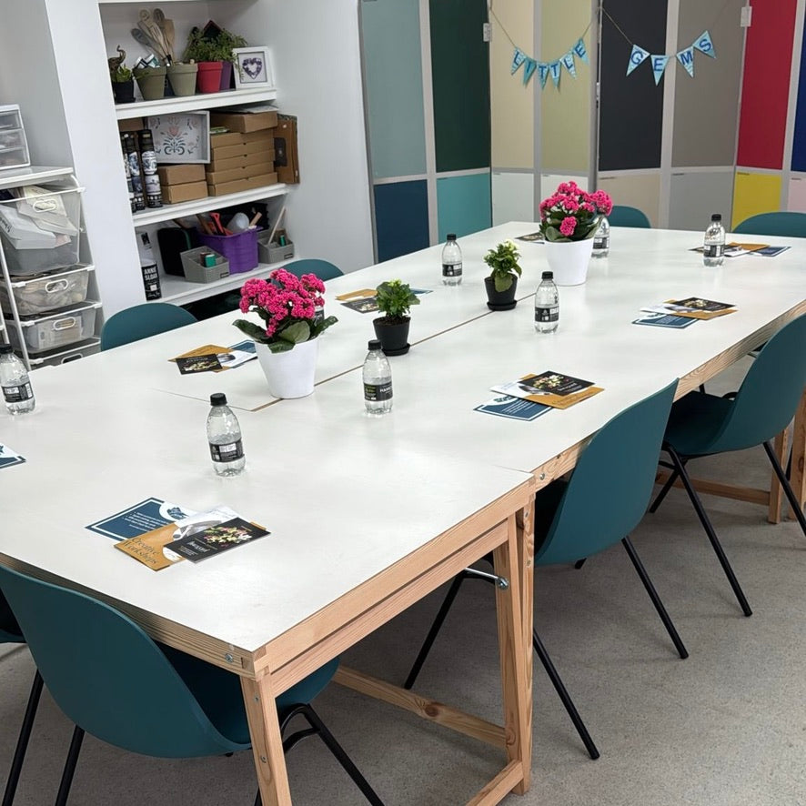 Meeting room in a workshop space with a tables set for a creative course featuring chairs, water bottles, and floral arrangements.