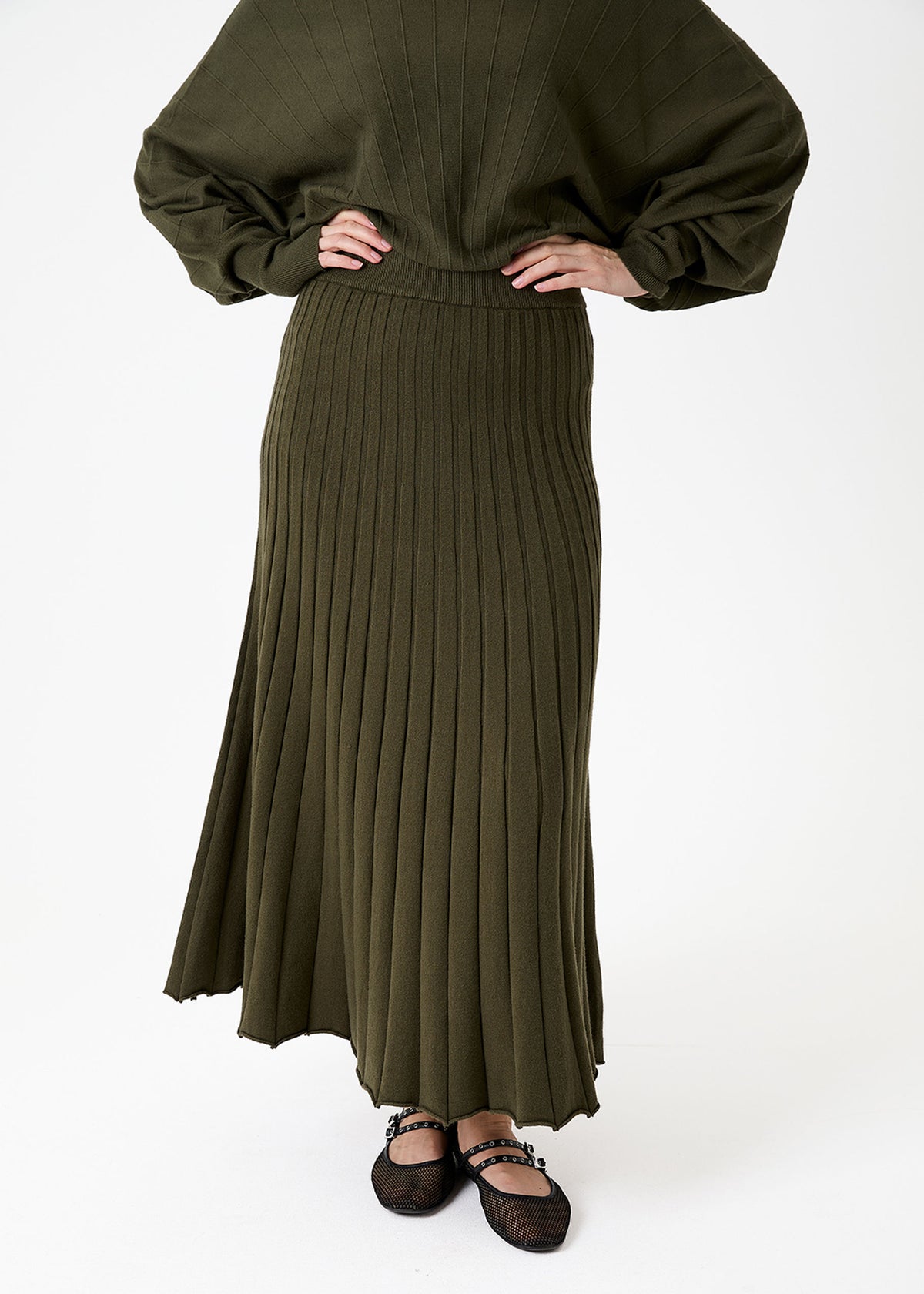 Cashmere Like Pleated Skirt Forest Khaki Green A model wearing an olive green pleated maxi skirt and matching long-sleeve top, paired with dark brown shoes, against a plain white studio background.