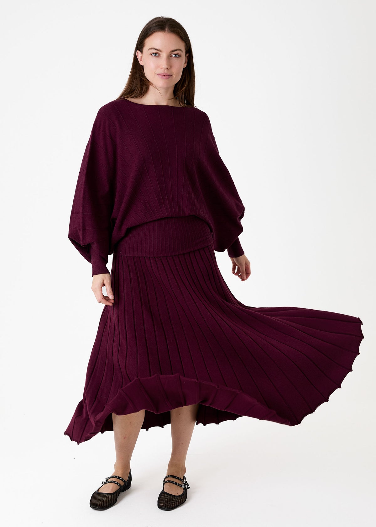Cashmere Like Pleated Skirt Merlot. A woman modeling a deep burgundy knit two-piece set consisting of a wide-sleeved top and a pleated midi skirt, shown against a plain white studio background.