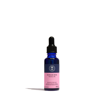 Damask Rose Facial Oil from Neal's Yard Remedies in a cobalt blue glass dropper bottle with a black cap and a pink label, set against a plain white background.