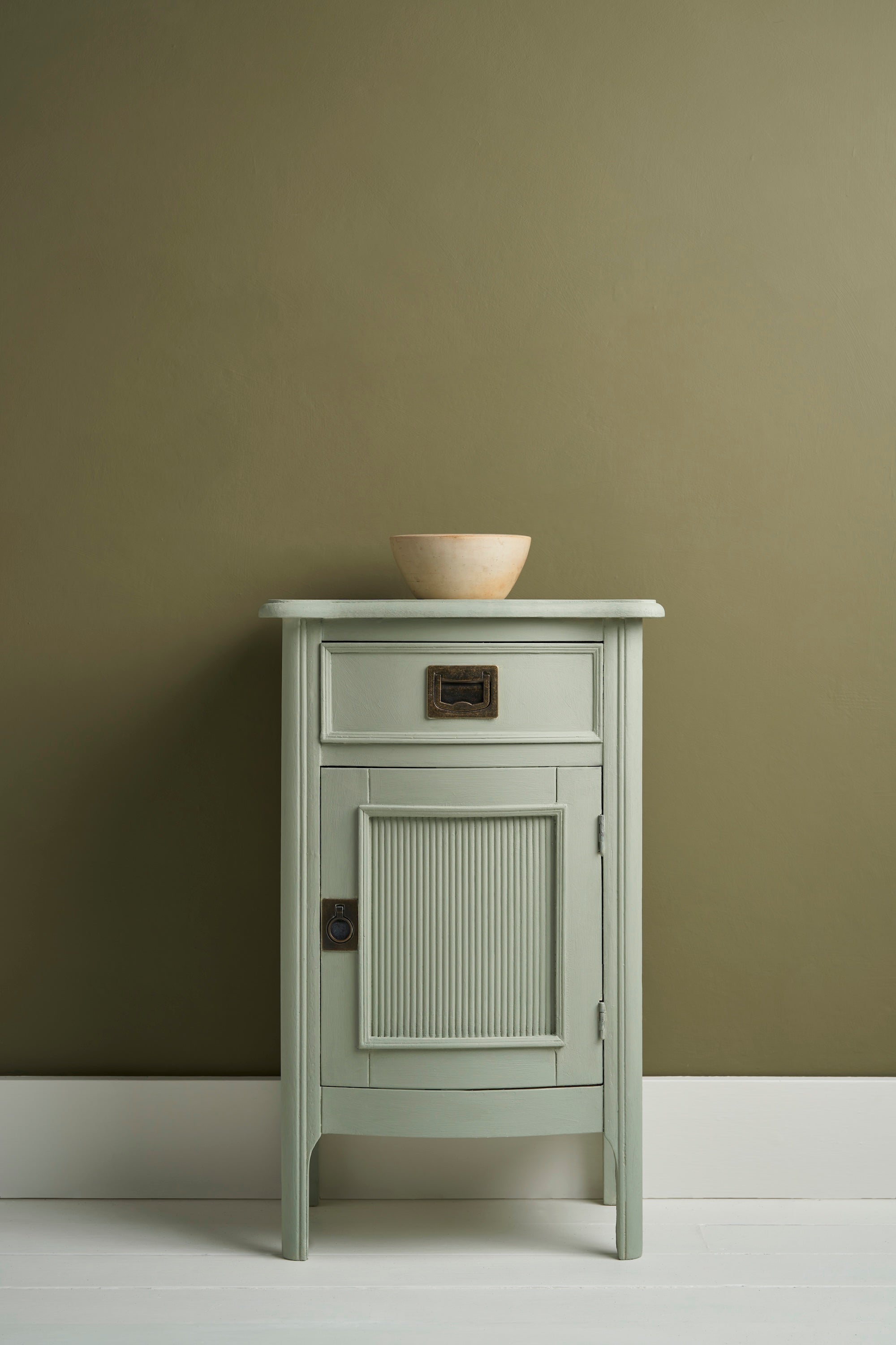 Attractive cabinet with ribbed front and brass handles painted in Annie Sloan Coolabah Chalk Paint against a wall paitted with Olive wall paint